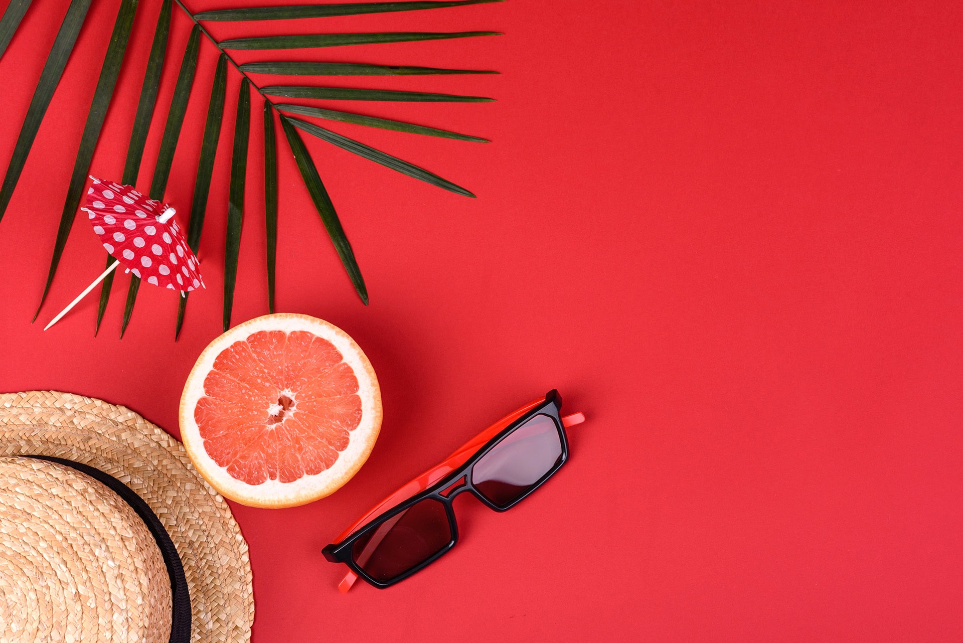 Sommerliche Drucksachen, Sonnenbrille, Hut, Grapefruit und Palme auf rotem Hintergrund.